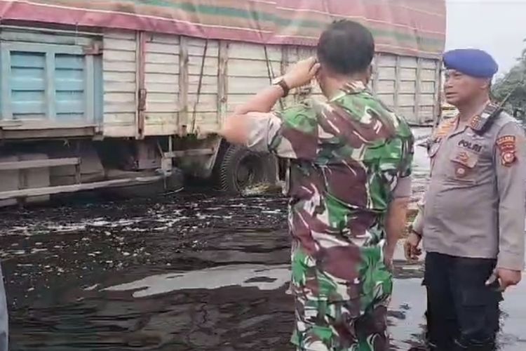 Polisi dan anggota TNI memantau kendaraan yang melintas di jalan lintas sumatera yang digenangi air, di Kabupaten Pelalawan, Riau, Jumat (5/1/2024).