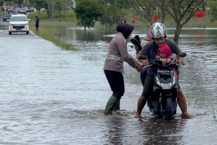 Kasatlantas Polres Pelalawan, AKP Akira Ceria mendorong motor warga yang mogok saat melewati jalan yang banjir, di Kecamatan Pangkalan Kerinci, Kabupaten Pelalawan, Riau, Rabu (27/12/2023).