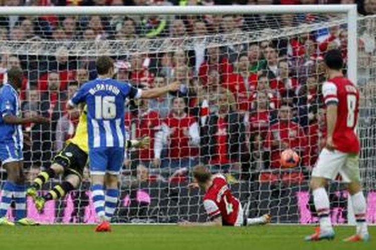 Bek Arsenal Per Mertesacker (kedua dari kanan) meloloskan bola ke sudut kiri bawah gawang Wigan Athletic, pada semifinal Piala FA, di Wembley, Sabtu (12/4/2014).