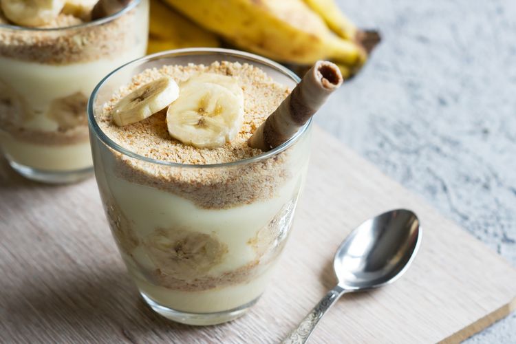Puding vanila pisang yang lembut dan manis dengan irisan pisang segar, disajikan dalam mangkuk kaca cantik untuk hidangan penutup yang menggugah selera