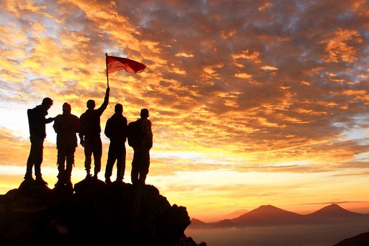 Ilustrasi pemuda. Sekelompok anak muda memegang bendera merah putih di puncak gunung, menatap matahari terbit. 