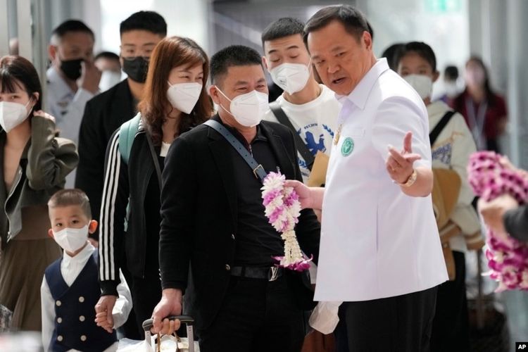 Menteri Kesehatan Masyarakat Thailand Anutin Charnvirakul (kanan), memberikan karangan bunga kepada wisatawan China setibanya di Bandara Internasional Suvarnabhumi, provinsi Samut Prakarn, Thailand, pada Senin (9/1/2023).