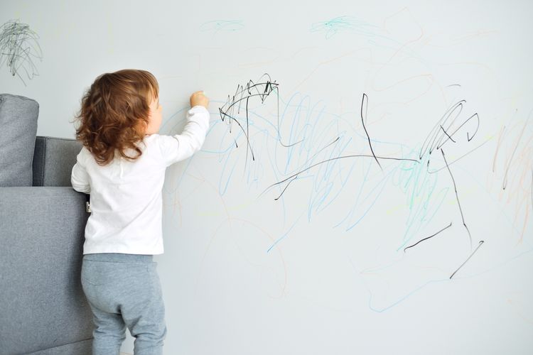 Ilustrasi anak mencoret-coret dinding dengan pulpen sehingga membuat dinding kotor dengan noda tinta.