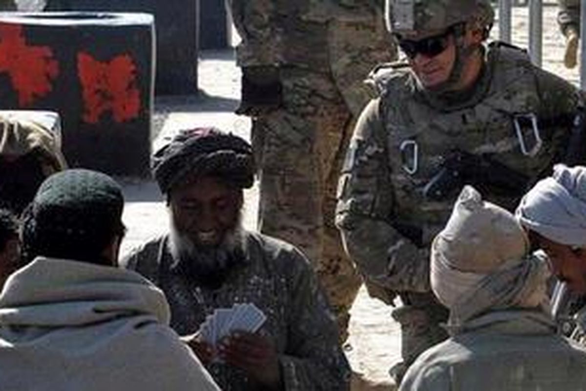 Seorang tentara Pasukan Bantuan Keamanan Internasional (ISAF) sedang menyaksikan beberapa pria Afganistan bermain kartu pada acara pembukaan sebuah klinik untuk korban perang di distrik Zharai, Afganistan.