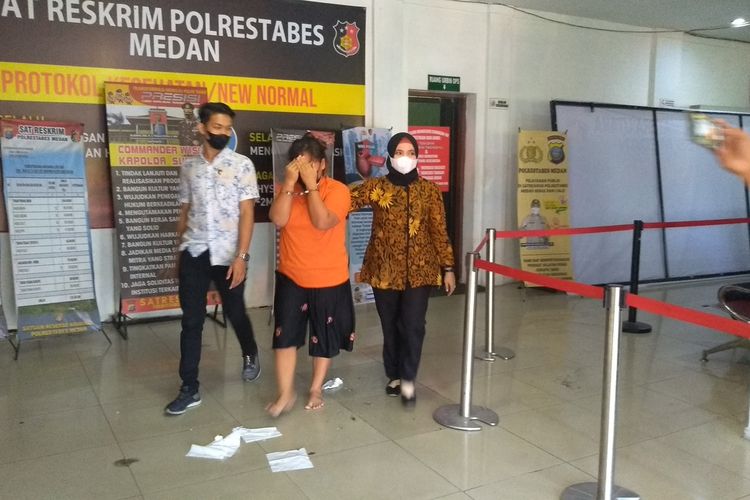 Tersangka LS (33) menutupi wajahnya saat digiring dari ruang pemeriksaan di Unit PPA Polrestabes Medan menuju sel tahanan pada Jumat (14/1/2022) pagi. Dia mengaku tiga kali memukul kepala anak angkatnya dengan penggaris besi dan sempat mengkompres wajah anaknya yang lebam pada pagi harinya dengan air panas dan induk kunyit.