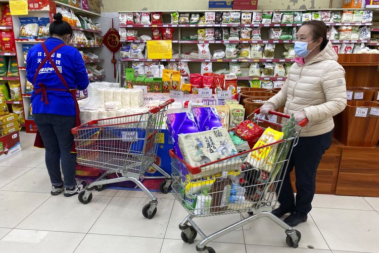Seorang wanita mengenakan masker mendorong kereta di dekat tanda yang menyerukan pembeli untuk waspada terhadap penyebaran virus corona, tidak mendengarkan desas-desus dan menghindari penimbunan di supermarket di Beijing, Cina, Rabu, 3 November 2021. 