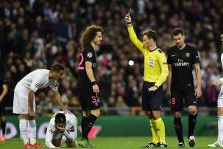 Wasit Mark Clattenburg (kuning) melayangkan kartu kuning kepada pemain belakang Paris Saint-Germain, David Luiz, setelah pelanggaran terhadap gelandang Real Madrid, Isco. Madrid menang 1-0 pada partai fase grup di Stadion Santiago Bernabeu, 3 November 2015.