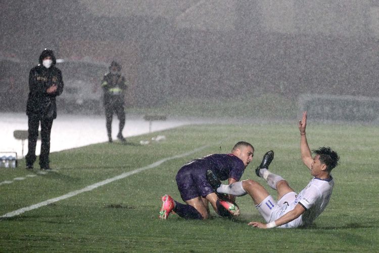 Pemain Persik Kediri Aldo Claudio dan pemain Arema FC Rizky Dwi terjatuh seusai duel pada pêrtandíngan pekan keduabelas Liga 1 2021-2022 yang diguyur hujan deras dan berakhir dengan skor 2-3 di Stadion Sultan Agung Bantul, Jumat (19/11/2021) malam.