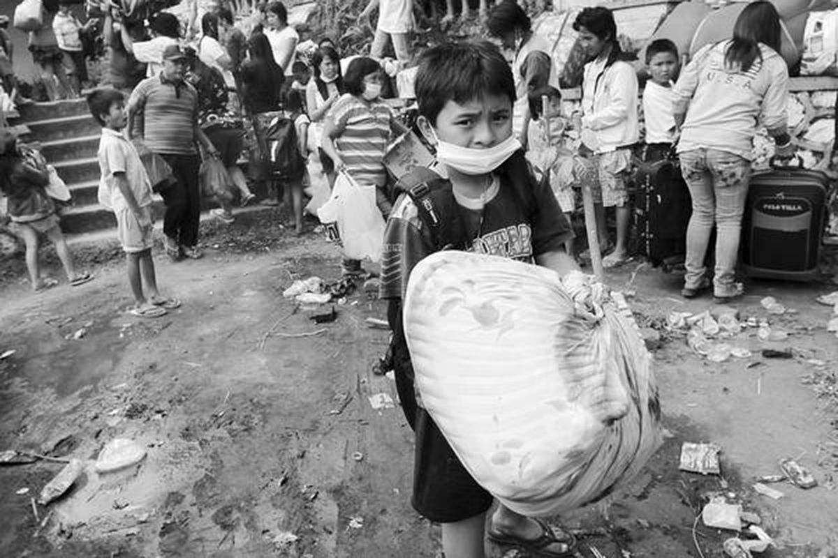Seorang anak laki-laki mengangkat barang bawaannya di sebuah lokasi penampungan sementara bagi pengungsi yang meninggalkan kediaman mereka karena meletusnya kembali Gunung Lokon di Tomohon, Sulawesi Utara, Minggu (17/7). Tidak ada laporan mengenai jatuhnya korban.