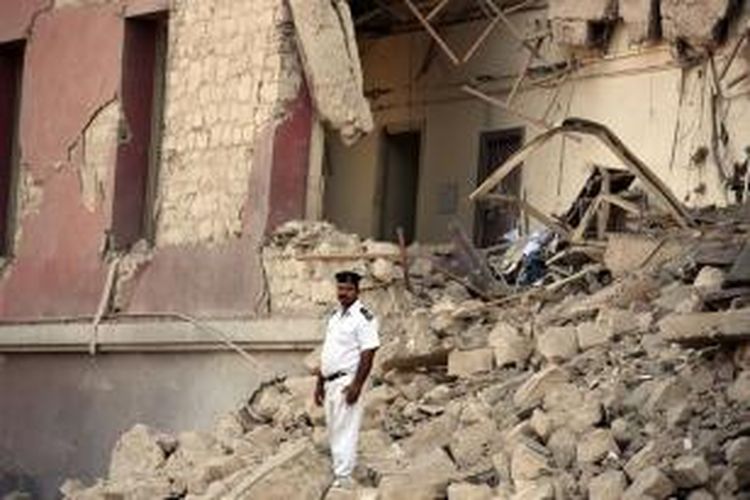 Seorang polisi Mesir berdiri di puing-puing dinding kantor konsulat Italia di Mesir yang dihantam serangan bom mobil, Sabtu (11/7/2015). ISIS mengaku mendalangi serangan tersebut.