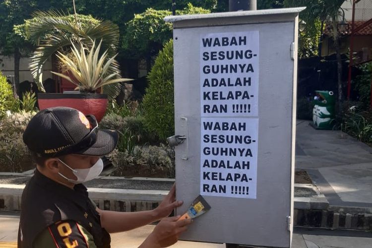 TERTIBKAN—Salah satu anggota Satpol PP Wonogiri membersihkan selebaran bertulisan wabah sesungguhnya ada kelaparan yang tertempel di fasilitas umum di Kota Wonogiri,  Senin (23/8/2021).