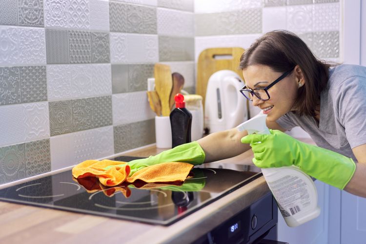 Ilustrasi wanita sedang membersihkan kompor kaca. 