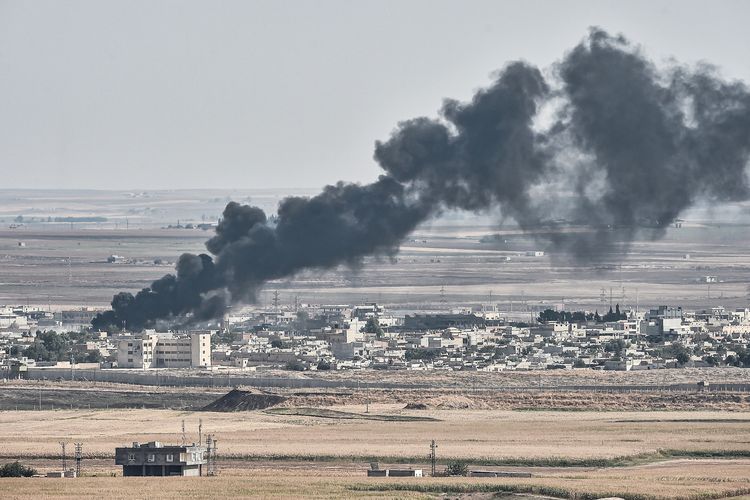 Gambar yang diambil pada 13 Oktober 2019 dari kota Turki Ceylanpinar menunjukkan asap mengepul dari kota perbatasan Suriah Ras al-Ain di tengah pertempuran antara Turki melawan Kurdi. Kurdi mengumumkan mereka menjalin kerja sama dengan pemerintah Suriah demi menghadapi Turki yang menyerang sejak 9 Oktober 2019.