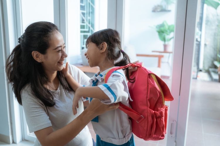 asian mother help her daughter to put the backpack on before going to school