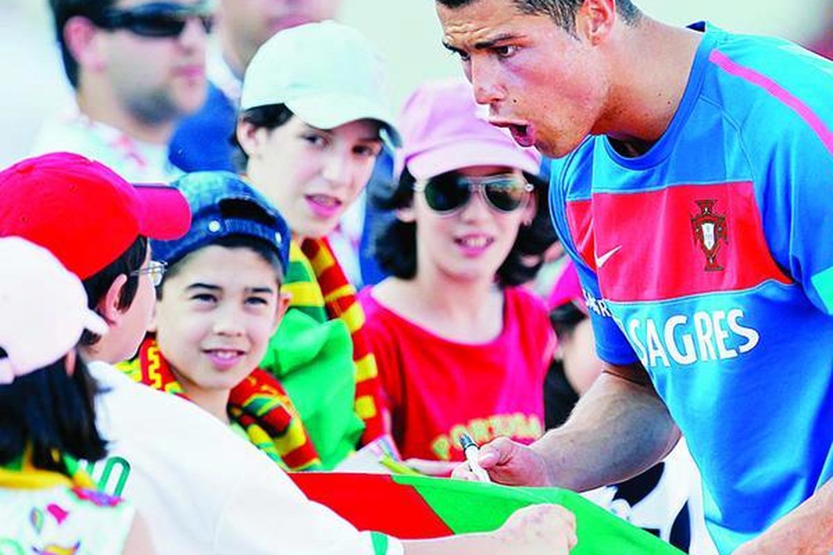Pemain termahal dunia, Cristiano Ronaldo, menandatangani bendera Portugal untuk penggemar cilik yang menunggunya pada sesi latihan tim di Covilha, Portugal, Minggu (23/5).