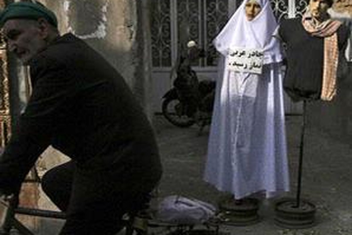 Seorang pria Iran bersepeda di depan dua maneken yang ditutup sesuai aturan berpakaian di Iran