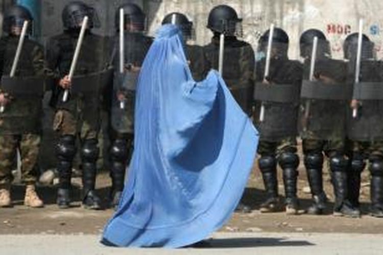 Seorang perempuan Afganistan yang mengenakan burka berjalan melintasi barisan polisi antihuru-hara di ibu kota Kabul.