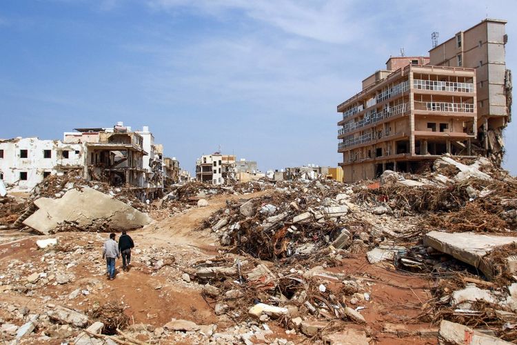 Beberapa pria berjalan melewati puing-puing bangunan yang disebabkan oleh banjir bandang di Kota Derna, Libya timur, pada 11 September 2023. Banjir bandang Libya timur menewaskan lebih dari 2.300 orang di kota pesisir Mediterania, Derna, saja, demikian ungkap layanan darurat pemerintah yang berbasis di Tripoli pada 12 September.