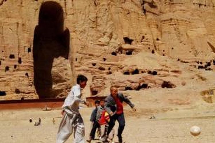 Anak laki-laki Afghanistan bermain sepak bola di depan area patung Buddha raksasa pernah berdiri di Provinsi Bamiyan, 9 April 2007. Patung-patung Buddha kuno dihancurkan oleh Taliban pada Maret 2000, meskipun ada protes internasional untuk menghentikan penghancuran.
