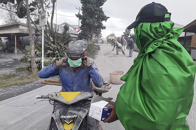 Warga membagikan masker kepada pengendara saat erupsi Gunung Sinabung di Karo, Sumatera Utara, Senin (10/8/2020). Gunung Sinabung erupsi dengan tinggi kolom 5.000 meter di atas puncak atau sekitar 7.460 meter di atas permukaan laut.