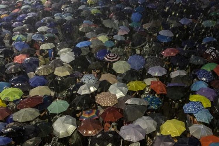 Para pengunjuk rasa pro-demokrasi menggunakan payung untuk menahan guyuran hujan saat mereka melakukan aksi duduk di pusat pemerintahan Hongkong mengecam sistem pemilihan pemimpin baru kota itu yang dinilai tidak demokratis.