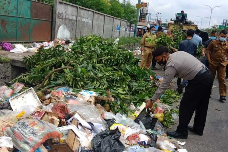 Petugas kepolisian Polsek Tampan turun tangan membersihkan sampah yang berserakan di Jalan HR Soebrantas, Kecamatan Tampan, Kota Pekanbaru, Riau, Selasa (5/1/2021).
