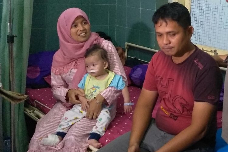 Muhammad Hasyim Nuril Aceh  (tengah) dan istrinya, Sabrina Tanjung, menggendong M Azmi yang masih diperban di bagian mulutnya setelah menjalani operasi bibir sumbing di Rumah Sakit Bhayangkara Medan, Selasa (18/6/2019).