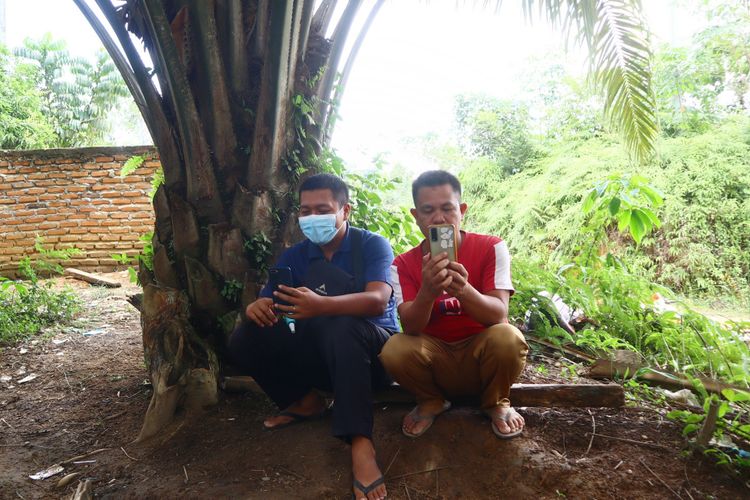 Warga Dusun Baru Kecamatan Pelepat mencari sinyal di bawah pohon sawit. Lokasi ini selalu ramai pada jam-jam tertentu karena warga ingin menelpon atau sekadar melihat sosial media.