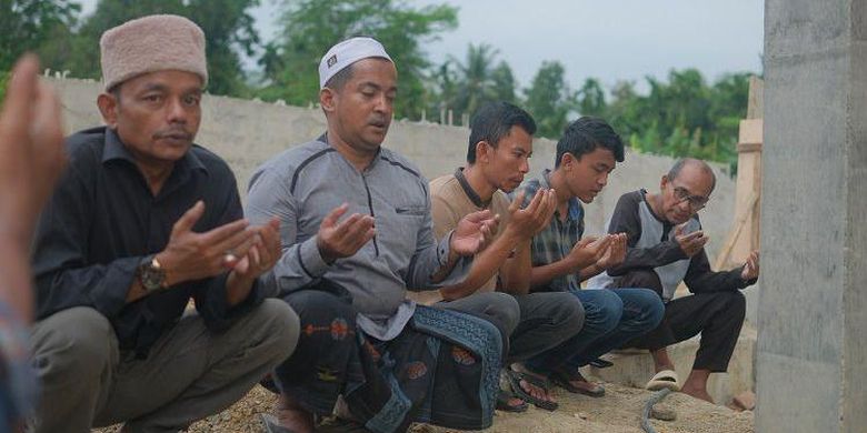 Tokoh yang disegani di Desa Bili Aron, Teungku Faisal (kopiah putih) bersama warga berdoa di dekat monumen Rumoh Geudong, pada Selasa, 26 Maret 2024.