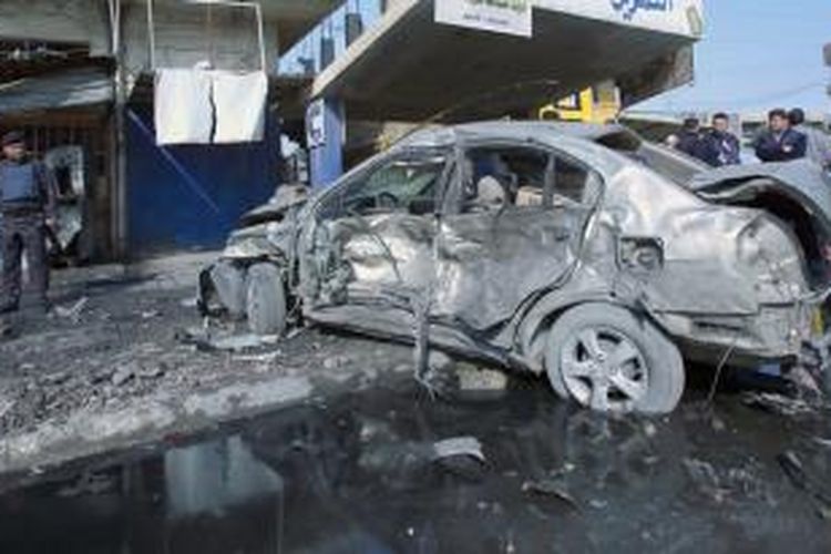 Seorang polisi Irak memerhatikan bangkai mobil yang hangus akibat bom di pusat kota Baghdad, Rabu (15/1/2013). Serangkaian serangan bom di Baghdad dan Baquba menewaskan sedikitnya 59 orang.