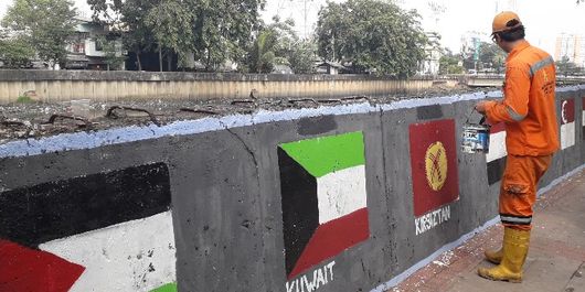 Petugas Penanganan Prasarana dan Sarana Umum (PPSU) Rawa Buaya membuat mural di tembok jalan pembatas Kali Mookervart, Jakarta Barat pada Senin (30/7/2018).