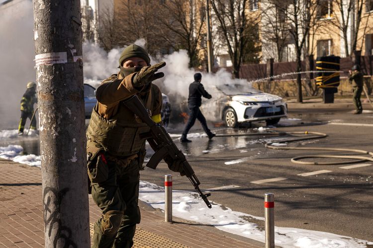 Tentara Ukraina mengambil posisi di luar fasilitas militer saat dua mobil terbakar, di sebuah jalan di Keiv, Ukraina, Sabtu, 26 Februari 2022. 