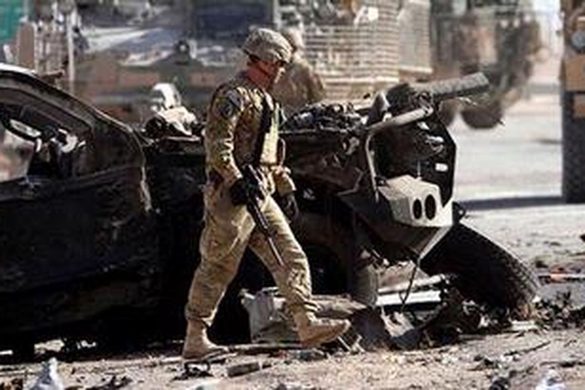 Seorang tentara Amerika Serikat melewati sebuah kendaraan yang hancur akibat bom bunuh diri di Kandahar, Afganistan, Kamis (19/1/2012).