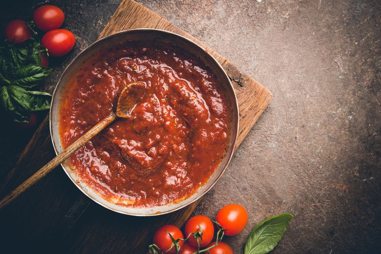 Mangkuk saus tomat segar dengan daun basil di atasnya, menunjukkan warna merah cerah dan tekstur kental yang sempurna untuk pasta
