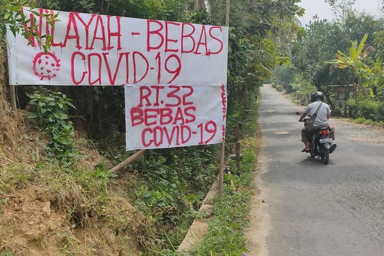 Warga mengganti spanduk peringatan dengan tulisan RT 32 Terbebas dari Covid di Pedukuhan Kadigunung, Kalurahan Hargomulyo, Kapanewon Kokap, Daerah Istimewa Yogyakarta.