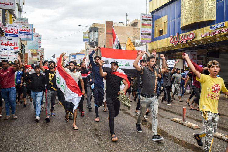 Para demonstran Irak berlari membawa bendera nasional dalam demonstrasi menentang pemerintah yang terjadi di Nasiriyah, ibu kota Provinsi Dhi Qar, pada 25 Oktober 2019.