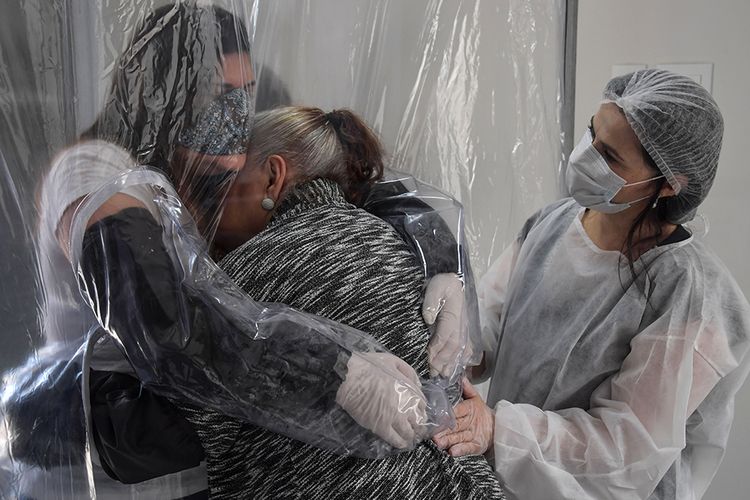 Suzane Valverde (kiri) memeluk ibunya, Carmelita Valverde (85), melalui tirai plastik transparan di sebuah panti jompo di Sao Paulo, Brasil, Sabtu (13/6/2020). Melepas rindu di tengah pandemi, orang-orang menggunakan tirai plastik sebagai solusi memeluk tanpa bersentuhan langsung guna meminimalisir risiko penularan virus corona (Covid-19).