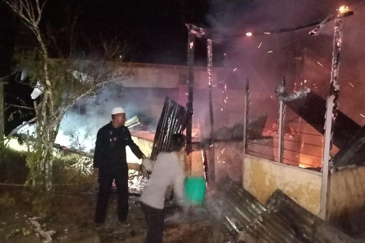 Dua anggota polisi mencoba memadamkan dua rumah warga Kariu, Kecamatan Pulau Haruku, Kabupaten Maluku Tengah yang terbakar pada Minggu malam (10/4/2022)
