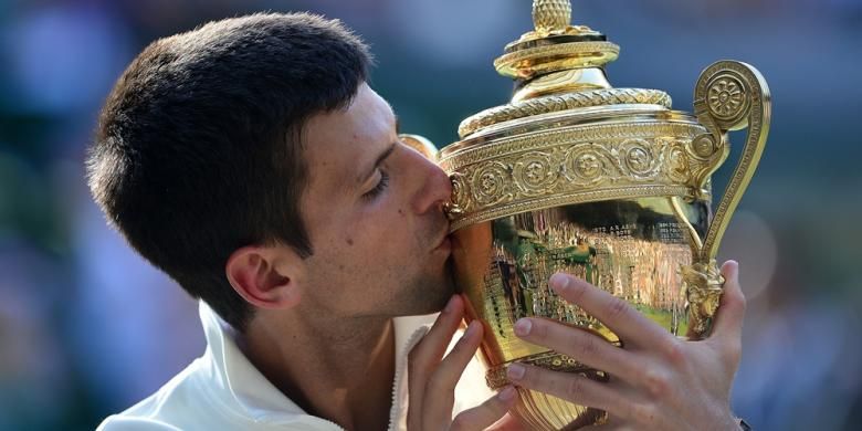 Petenis Serbia, Novak Djokovic, mencium trofi juara Wimbledon yang dia dapatkan setelah mengalahkan petenis Swiss, Roger Federer, pada partai final yang berlangsung di All England Tennis Club, London, Minggu (6/7/2014). Djokovic menang 6-7 (7), 6-4, 7-6 (4), 5-7, 6-4.