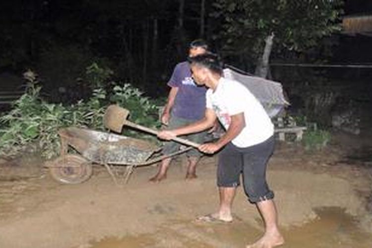 Dua warga di Jorong Sei (Sungai) Pangkua, Nagari Pakan Rabaa, Kecamatan Koto Parik Gadang Diateh, Kabupaten Solok Selatan, Sumatera Barat, Jumat (14/12/2012) malam tengah membersihkan pelataran rumah dari material pasir dan lumpur setelah dilanda banjir bandang atau galodo. Galodo menghantam kawasan perkampungan itu antara Kamis (13/12/2012) malam hingga menjelang Jumat (14/12/2012) dinihari. 