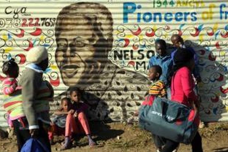 Orang-orang berjalan melewati mural mantan presiden Afrika Selatan Nelson Mandela, 26 Juni 2013 di Soweto, saat mantan presiden itu menjalani hari ke-19 di rumah sakit jantung Mediclinic di Pretoria. Warga berkumpul di luar rumah sakit tempat Nelson Mandela terbaring kritis.