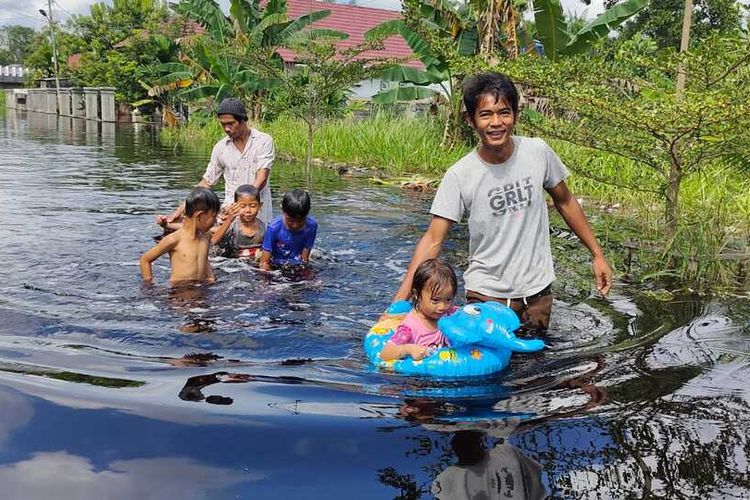 Warga membawa anak-anakya mengarungi banjir untuk pergi ke rumahnya di Kelurahan Bumi Ayu, Kecamatan Dumai Selatan, Kota Dumai, Riau, Sabtu (30/10/2021).