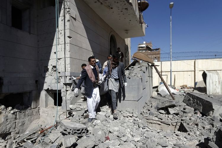 Warga Yaman berjalan di reruntuhan penjara yang diserang oleh koalisi pimpinan Arab Saudi dalam sebuah operasi udara. Akibat serangan tersebut, 12 orang yang semuanya tahanan dilaporkan tewas. (13/12/2017)