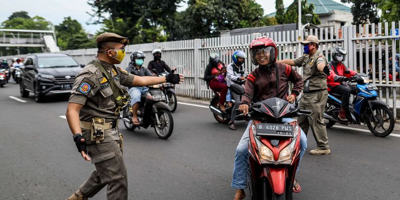 Petugas satuan polisi pamong praja menghentikan pengendara motor yang tidak menggunakan masker saat patroli penegakan aturan pembatasan sosial berskala besar (PSBB) di Jl. Matraman Raya, Kecamatan Jatinegara, Jakarta Timur, Selasa (19/5/2020). Dalam kegiatan patroli PSBB tersebut, target penegakan untuk masyarakat yang tidak mengunakan masker dijalanan.