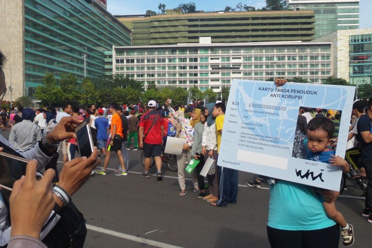 Seorang warga mengabadikan foto dengan menggunakan “KTP Anti Korupsi” di Bundaran Hotel Indonesia, Minggu (19/3/2017). Pengusutan kasus e-KTP saat ini telah masuk ranah pengadilan. Ada sejumlah nama besar yang disebut di dalam surat dakwaan kasus tersebut.