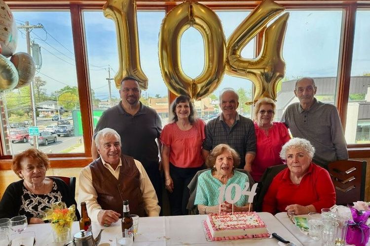 Antoinette Inserra perempuan berusia 104 tahun meniup lilin ulang tahunnya dikelilingi oleh keluarganya.
