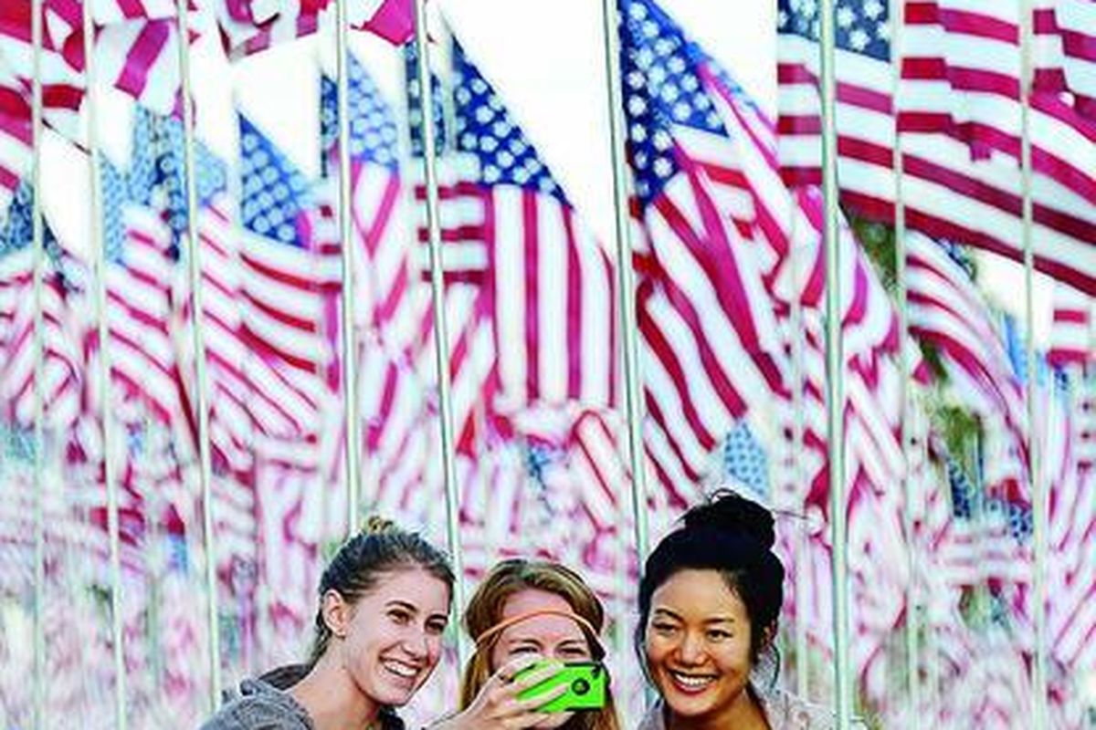 Tiga mahasiswa  berfoto dengan latar belakang bendera Amerika Serikat yang dipasang mahasiswa dan staf Pepperdine University, Malibu, Minggu (9/9), untuk mengenang tragedi 11 September 2001.