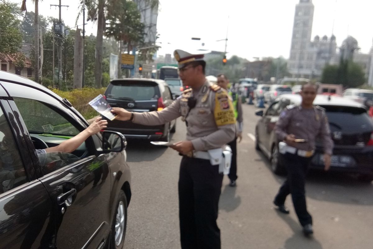 Seorang petugas kepolisian sedang membagikan flyer di Simpang Gadog, Ciawi, Sabtu (12/10/2019). Hal tersebut dilakukan sebagai bentuk sosialisasi pelaksanaan sistem 2-1 yang akan diuji coba pada tanggal 27 Oktober 2019 mendatang.