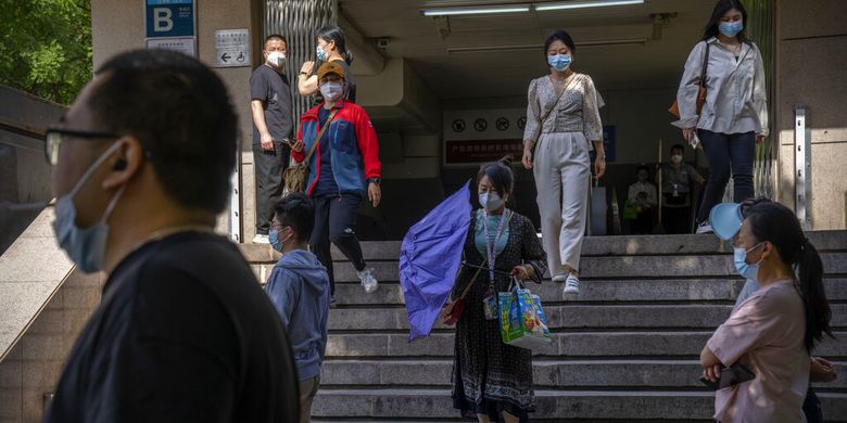 Para komuter yang mengenakan masker berjalan menuruni tangga di stasiun kereta bawah tanah yang baru dibuka kembali di kawasan pusat bisnis di Beijing, Selasa, 31 Mei 2022. 