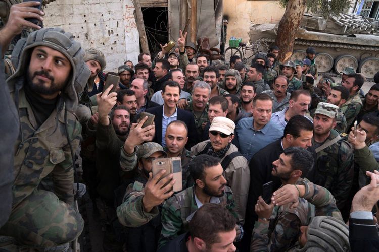 Sebuah gambar yang dirilis Kepresidenan Suriah di akun resmi Facebook, Minggu (18/3/2018), menunjukkan Presiden Suriah Bashar Al Assad berpose untuk foto dengan pasukan pemerintah di Ghouta Timur. (AFP)